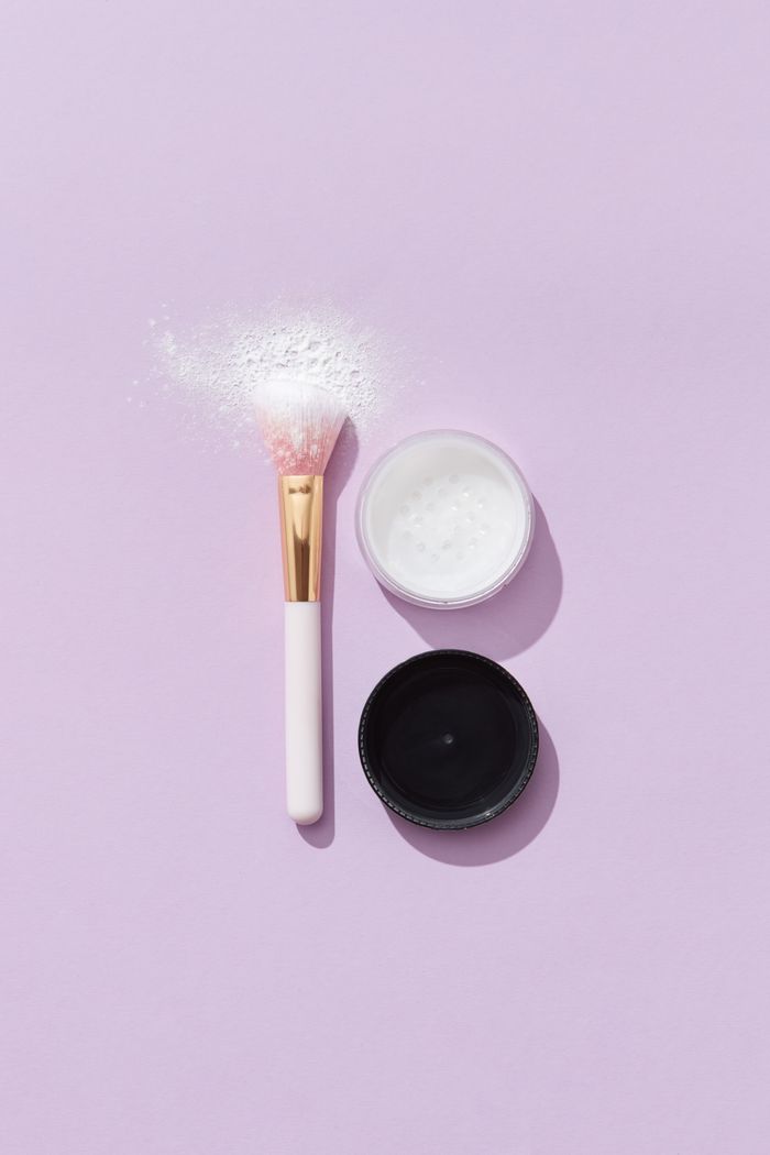 A minimalistic flat lay of a makeup brush with loose powder set against a pastel purple backdrop.